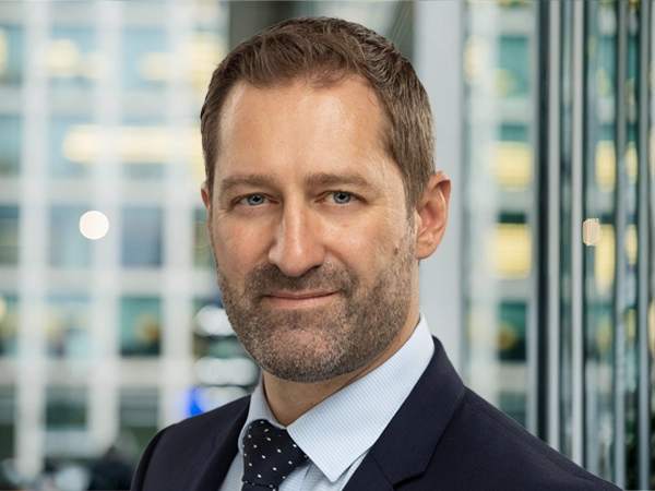 Portrait of Adam Ralph, Director, Dubai,  with city landscape featuring building with lots of windows in the background.