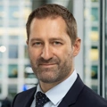 Portrait of Adam Ralph, Director, Dubai, with city landscape featuring building with lots of windows in the background.