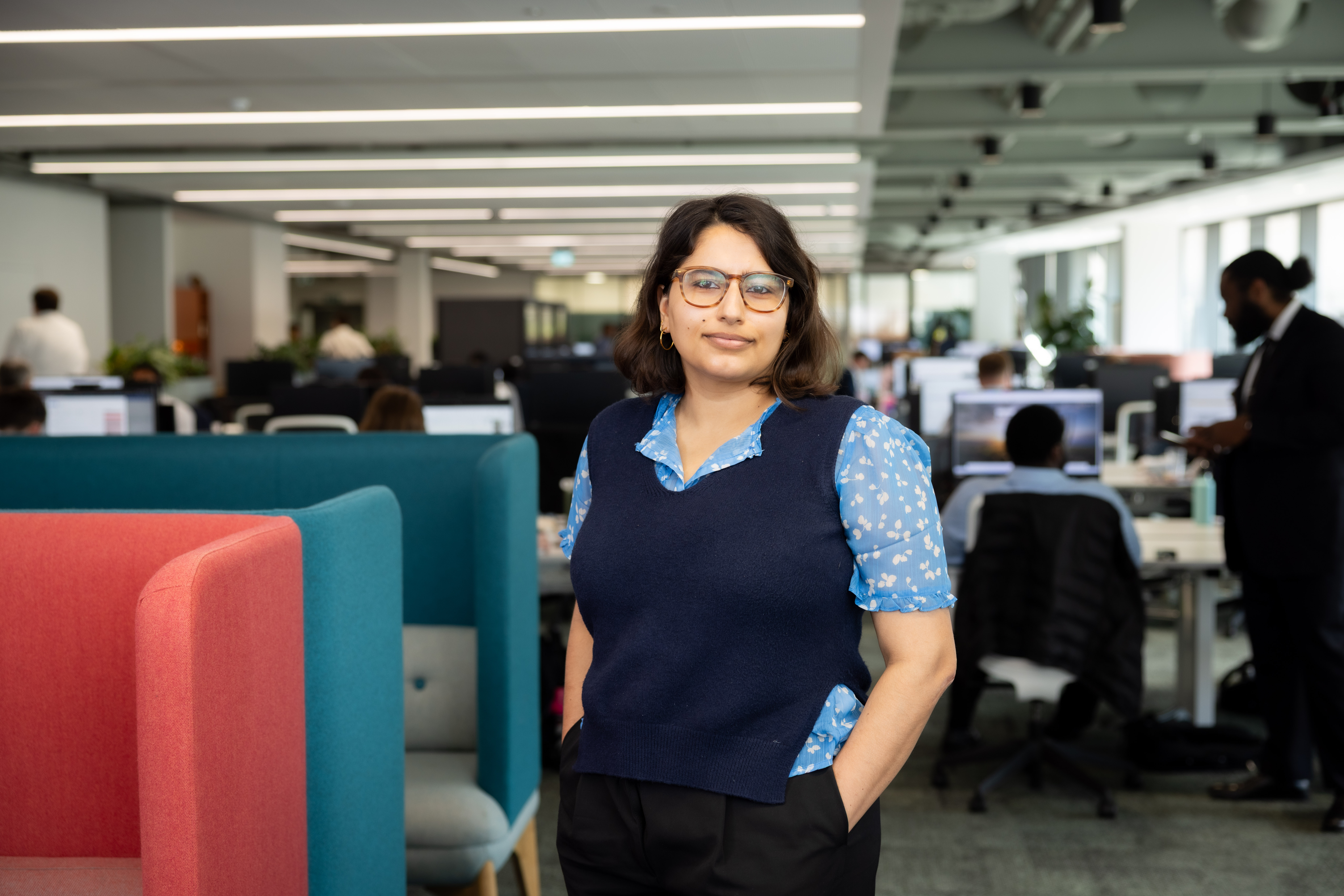 Portrait of Verriin Kaur, Global External Communications Manager, Standing in office against blue and orange chair.