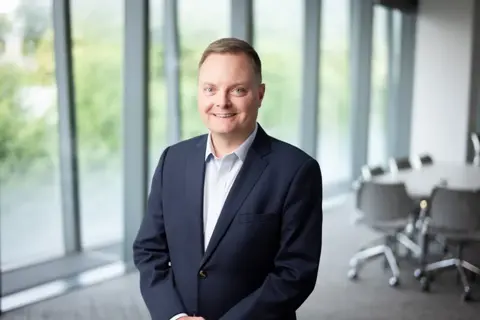 Portrait of Brian Shuptrine, Regional Managing Director, Asia, with city landscape featuring building with lots of windows in the background.