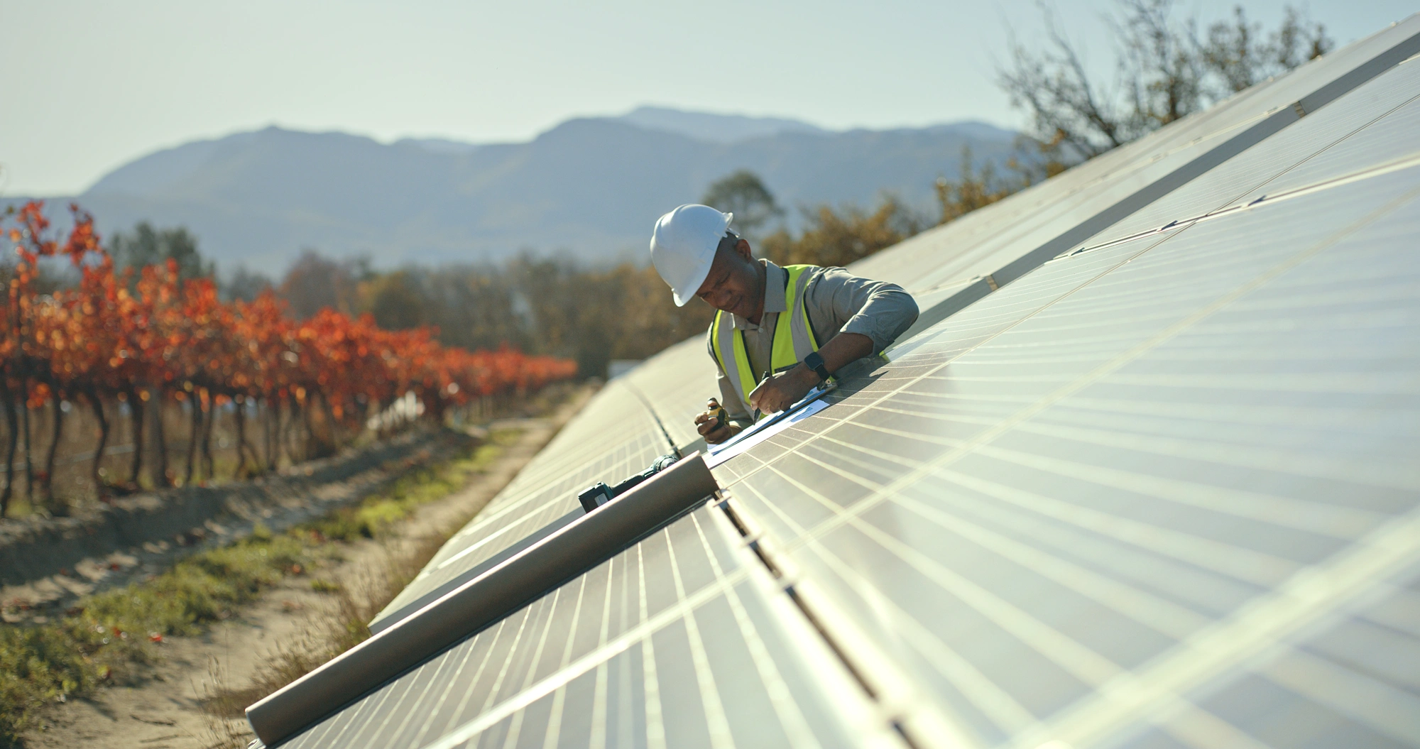 A workman working on a solar panel installation with trees and mountains in background, Kenya