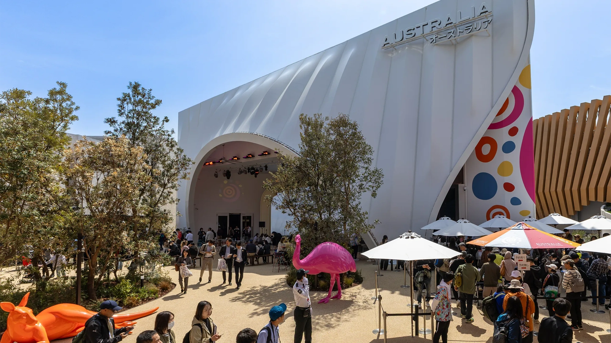 Australian and Japanese Expo at day time with blue skies and lots of visitors. There are colorful statue animals such as a orange kangaroo and pink flamingo.