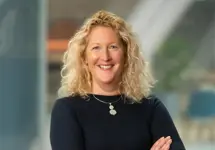 Portrait of Vicky Shepherd, Associate Director, UK Communications, standing with arms folded in office smiling