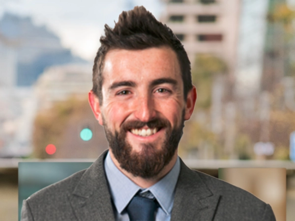 Kyle Stead outside in front of a blurred brown background featuring a building and mix of natural and urban elements.