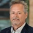 Portrait of Ron Staa, Director, outside in front of a blurred brown background featuring a building and mix of natural and urban elements.