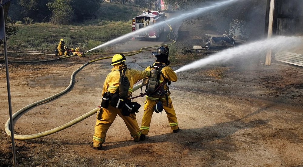 Fire fighters in yellow suits using a water hose