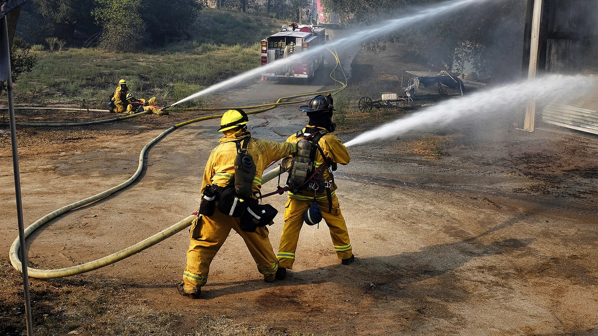 Fire fighters in yellow suits using a water hose