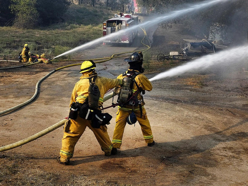 Fire fighters in yellow suits using a water hose