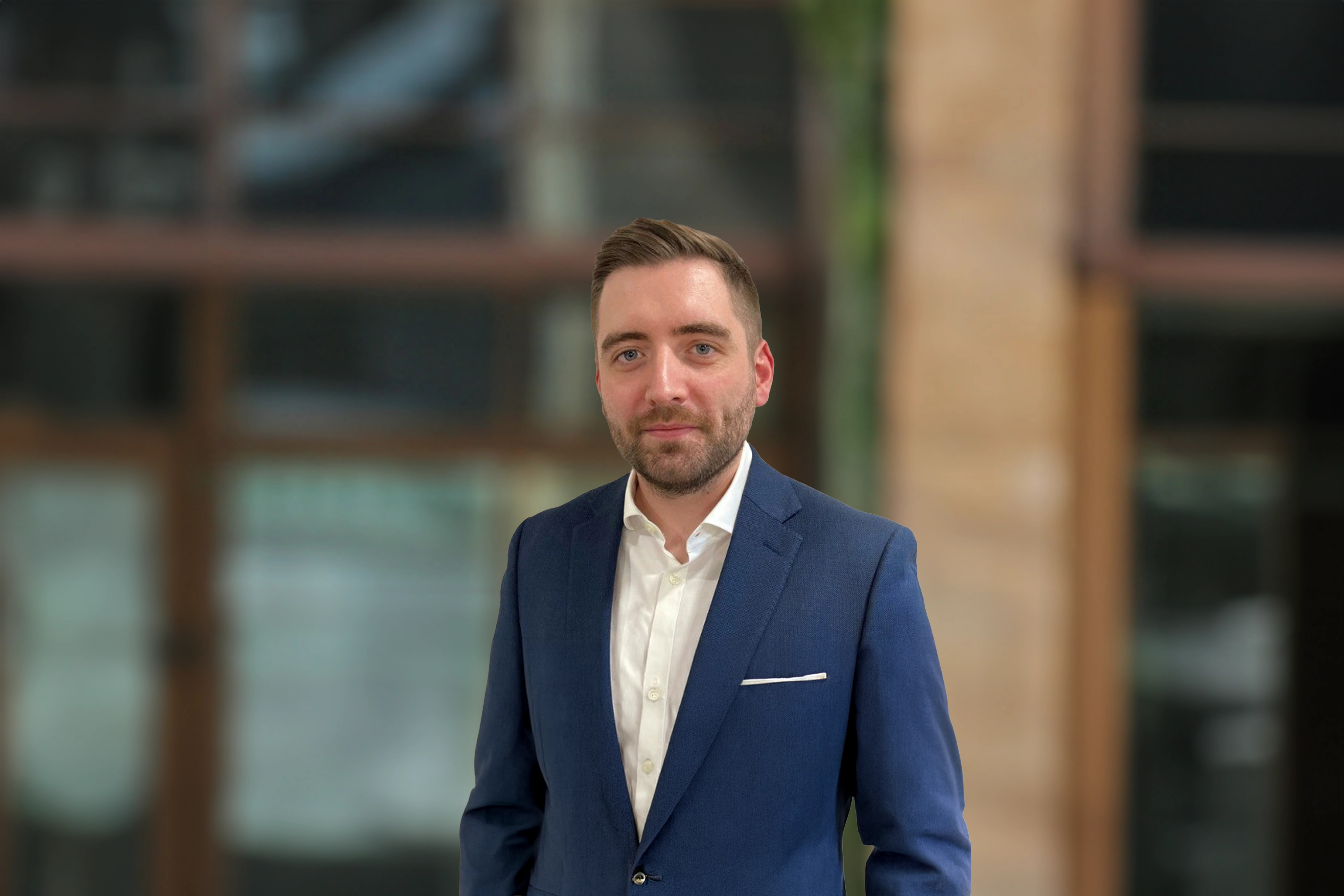 Paul Barry, outside in front of a blurred brown background featuring a building and mix of natural and urban elements.