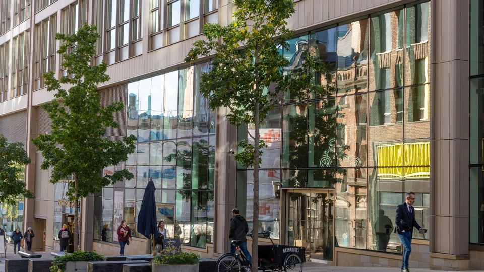 Image of glass window building with trees in front of it and people walking by