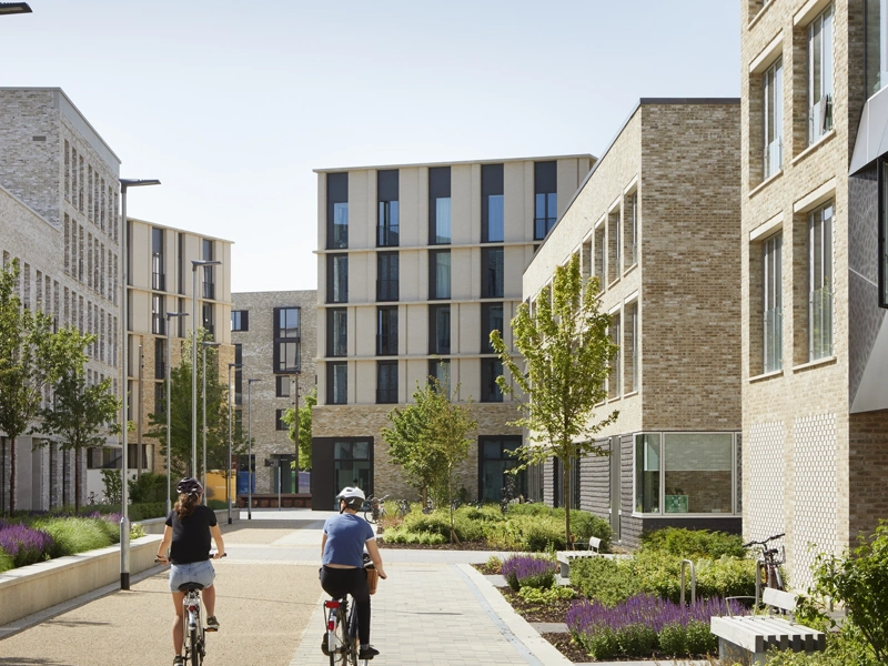 Daytime photo of a multi-storey residential development with two cyclists at the centre of the image, riding between buildings