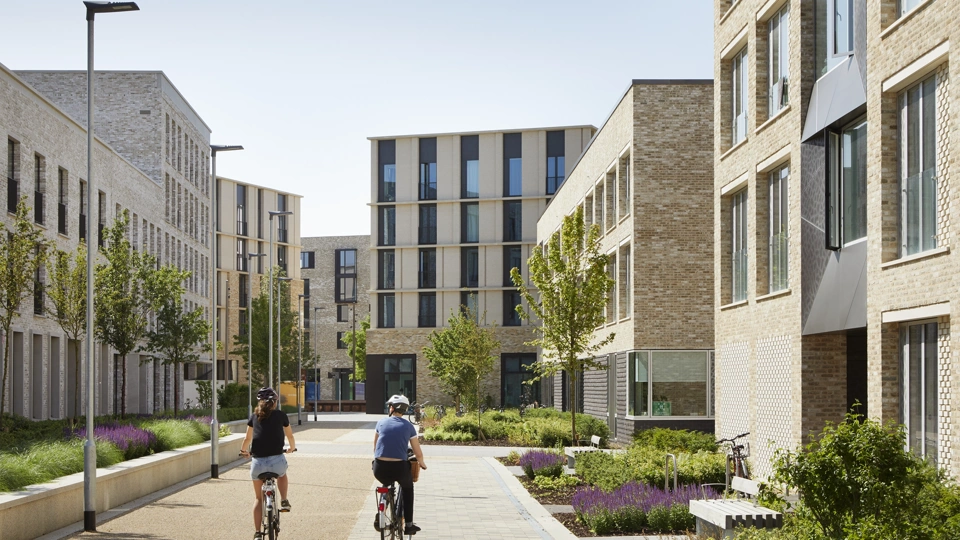 Daytime photo of a multi-storey residential development with two cyclists at the centre of the image, riding between buildings
