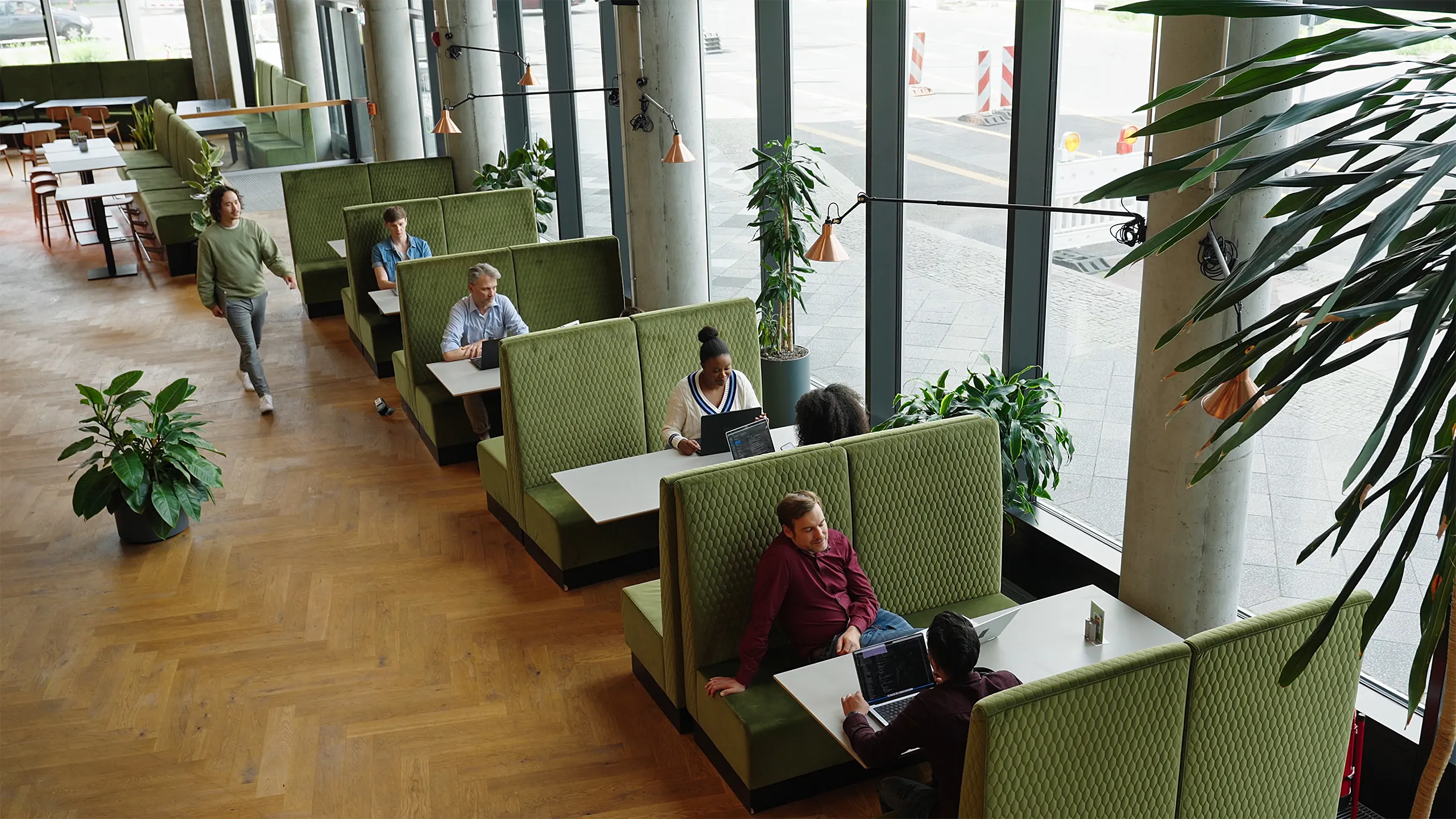 Modern office lounge with green booth seating, large windows and people working and meeting.