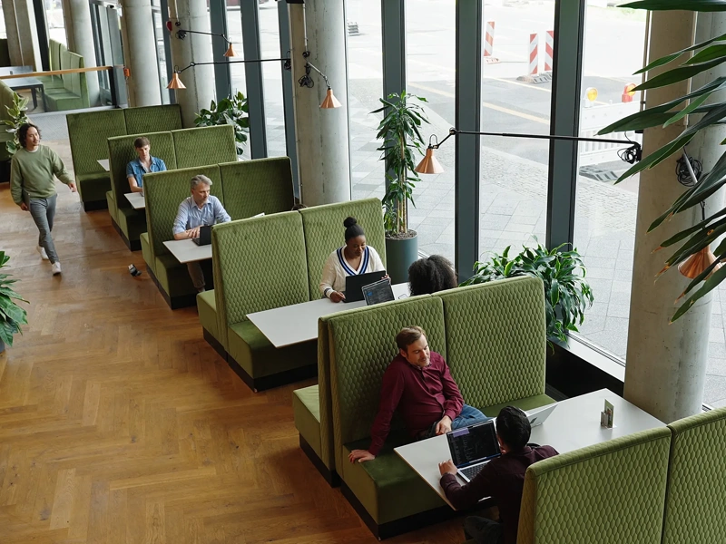 Modern office lounge with green booth seating, large windows and people working and meeting.