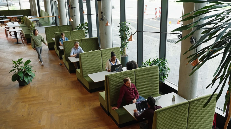 Modern office lounge with green booth seating, large windows and people working and meeting.