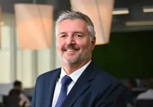 Portrait of Kobus Havemann, Country Manager, Smiling in blue suit in blue themed office space.