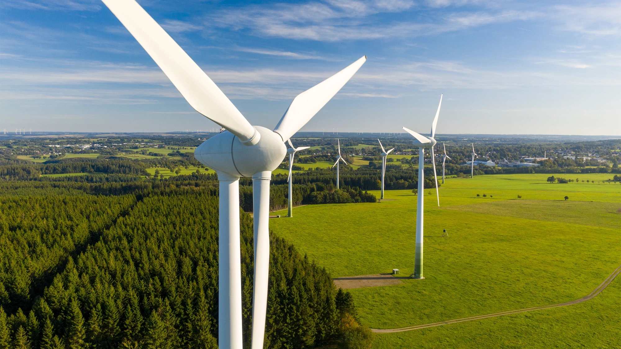 Big white wind turbines in sea water against blue sky.