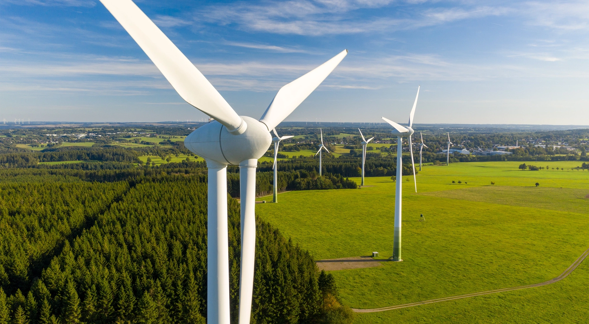 Big white wind turbines in sea water against blue sky.