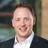 Portrait of Garry Murphy, UK Head of Project Management, Infrastructure, outside in front of a blurred brown background featuring a building and mix of natural and urban elements.