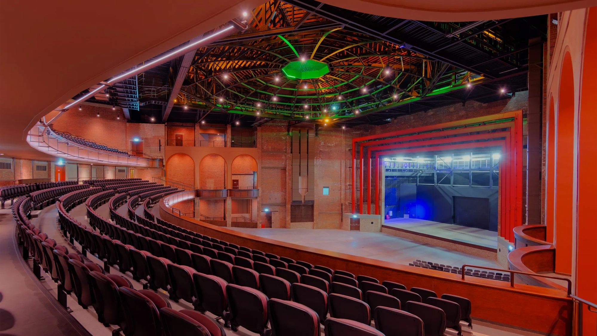 Bradford live, theater with red lights and ambiance, and green LED lights. there's a stage and chairs for the audience.