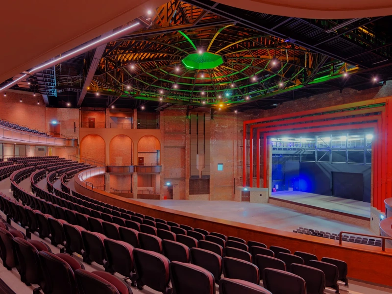 Bradford live, theater with red lights and ambiance, and green LED lights. there's a stage and chairs for the audience.
