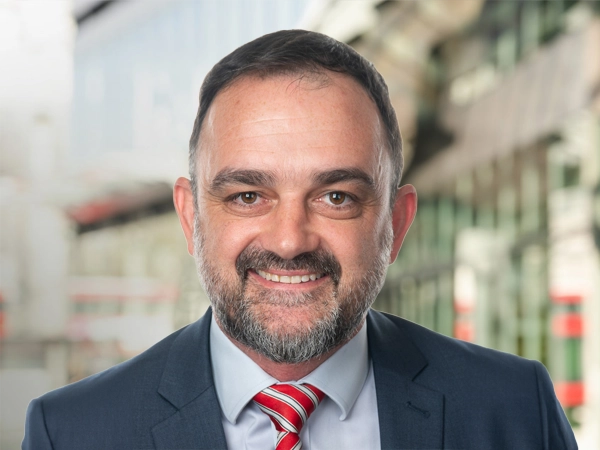 Brett Kalisch, Director, Natural Resources, Australia & New Zealand, standing outside in front of buildings featuring an urban cityscape with a mix of architectural styles. The scene includes some windows and red features, adding a touch of color.