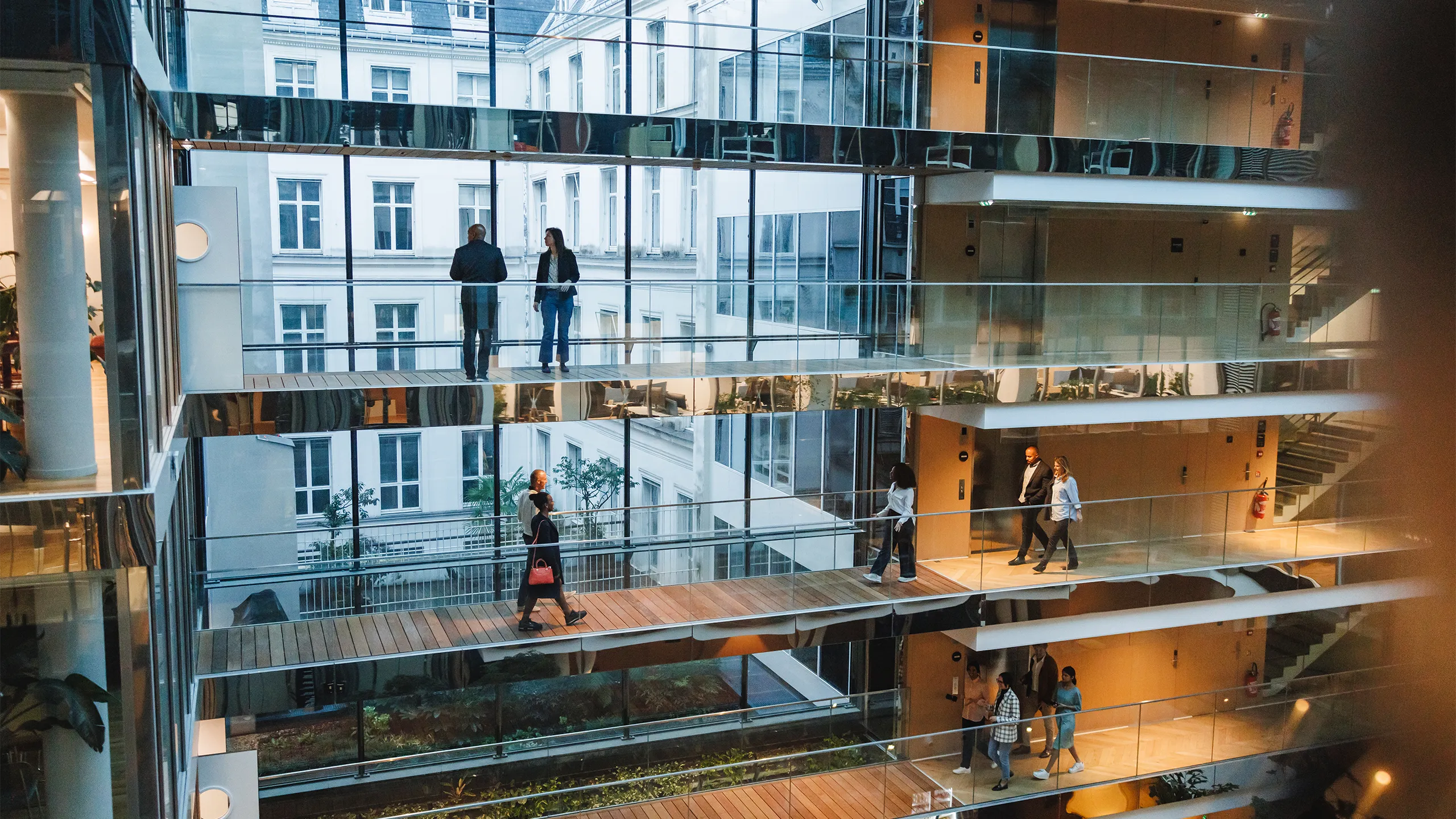 Open multi-storey office atrium with glass walkways and people walking between floors.