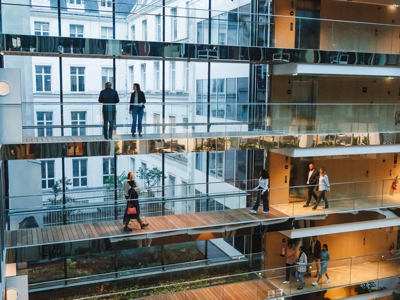 Open multi-storey office atrium with glass walkways and people walking between floors.