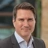 Portrait of Andrew Baker, Europe Lead, outside in front of a blurred brown background featuring a building and mix of natural and urban elements.