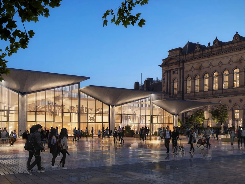 Modern glass-fronted pavilion with angular roofiines illuminated at dusk, set beside a historic stone building. People gather and walk across a reflective public square in front of the entrance.