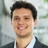 Portrait of Eduardo Carvalho, Senior Project Manager, Real Estate Brazil, standing outside in front of an outdoor urban setting, featuring modern architectural elements with clean lines. There are hints of greenery, suggesting some trees or plants.