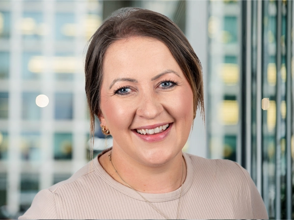 Portrait of Ashley Stewart, Project Director, with city landscape featuring building with lots of windows in the background.