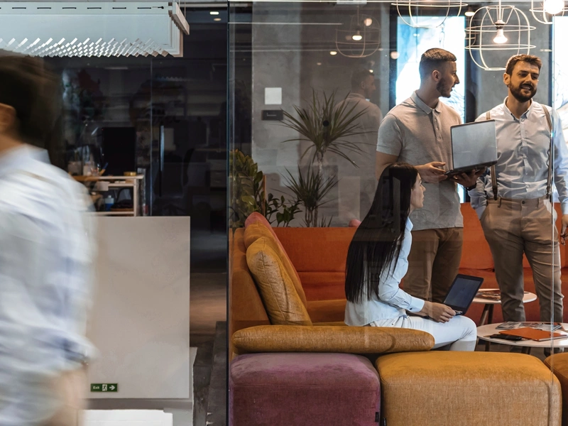 Colleagues standing around in a colourful based office, engaged in a conversation.
