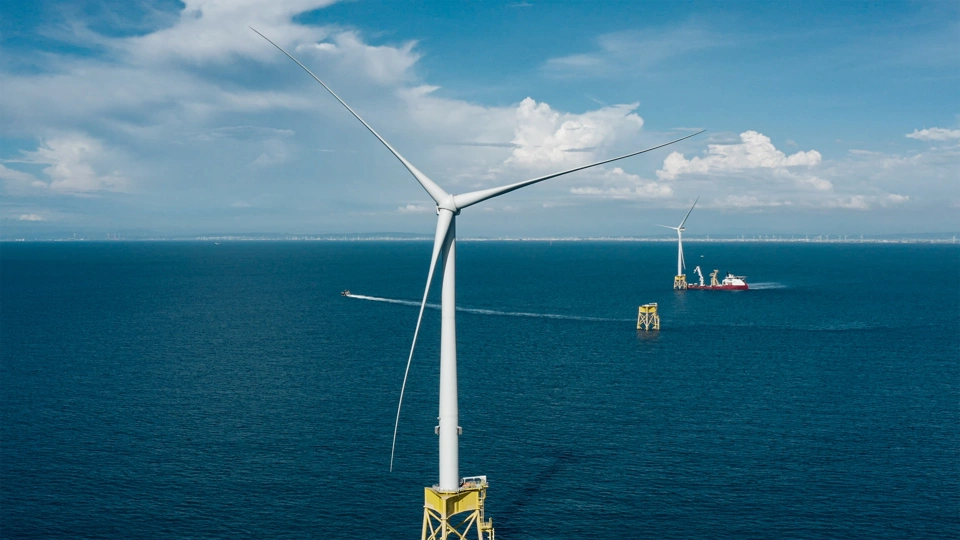 Daytime aerial view of an offshore wind turbine in the foreground with further turbines in the distance