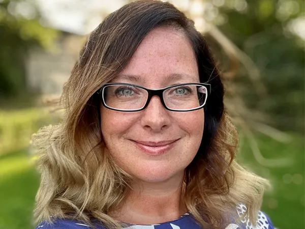 Portrait of Jessica Wergin, director, smiling in white shirt outside with green background.