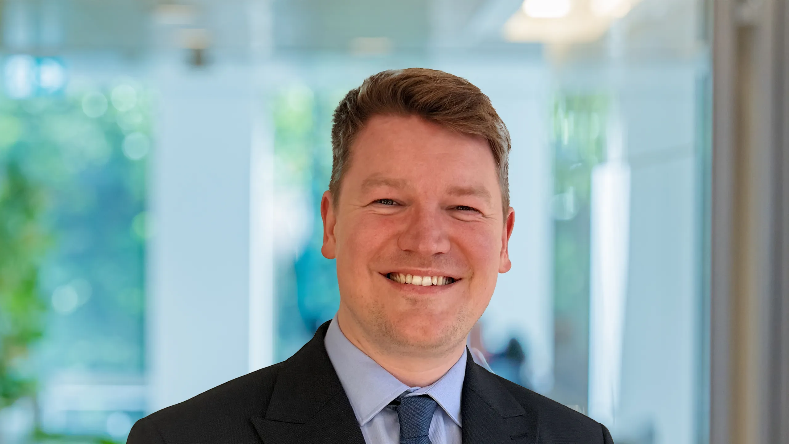 Portrait of Michael O’Connor Atkin, Sports and Venues Lead, Asia, standing in pant based office smiling.