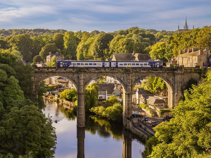 Train in Newcastle going over a bridge suspended over water in amongst leafy greenery