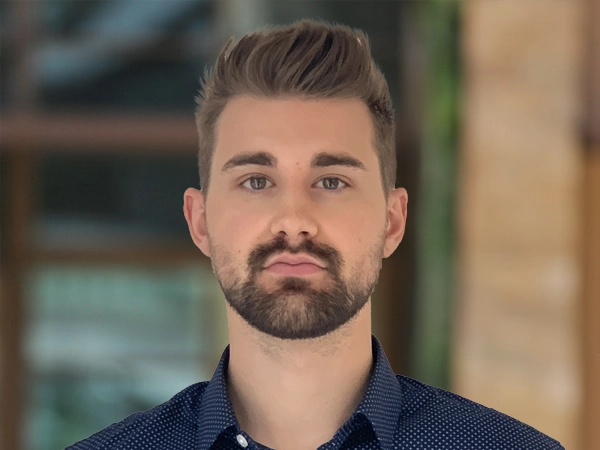 Portrait of Jay Figg, Senior Project Manager, Infrastructure, outside in front of a blurred brown background featuring a building and mix of natural and urban elements.