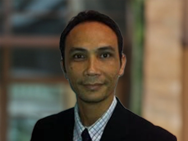 Portrait of Dargo Fitz Dinata, Director, Cost Management, Indonesia, outside in front of a blurred brown background featuring a building and mix of natural and urban elements.