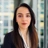 ortrait of Gabriela Mariniuc, Associate Director, standing in window based office building smiling.
