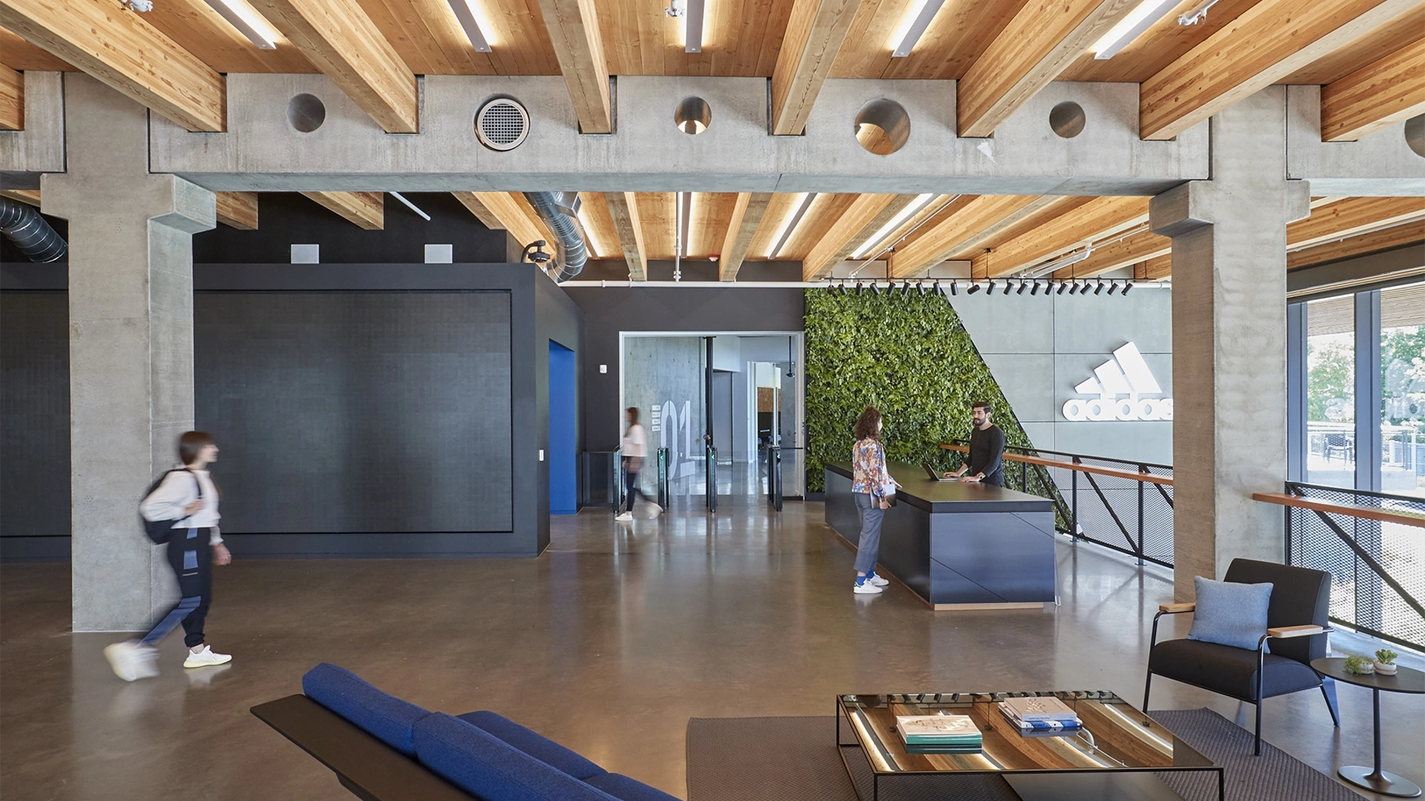 Modern Adidas offices with wooden interior and two people walking while a woman talks to a man at a reception desk