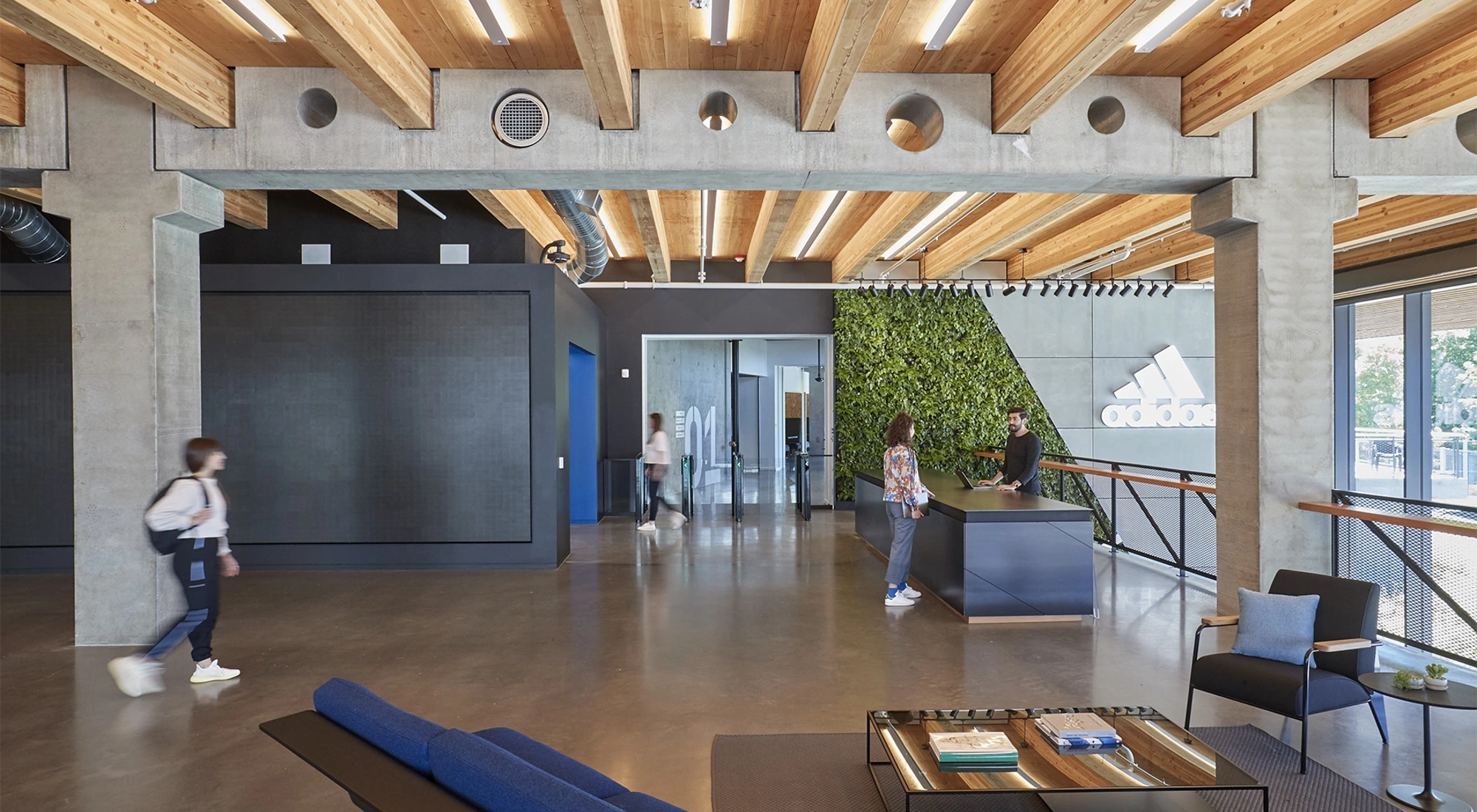 Modern Adidas offices with wooden interior and two people walking while a woman talks to a man at a reception desk