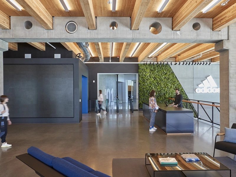 Modern Adidas offices with wooden interior and two people walking while a woman talks to a man at a reception desk