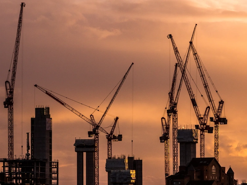 Color image depicting cranes and heavy duty construction equipment on the London skyline as the sun sets. The cranes have been busy constructing blocks of flats and apartments to ease the housing crisis in London and the south east of England. Lots of room for copy space.