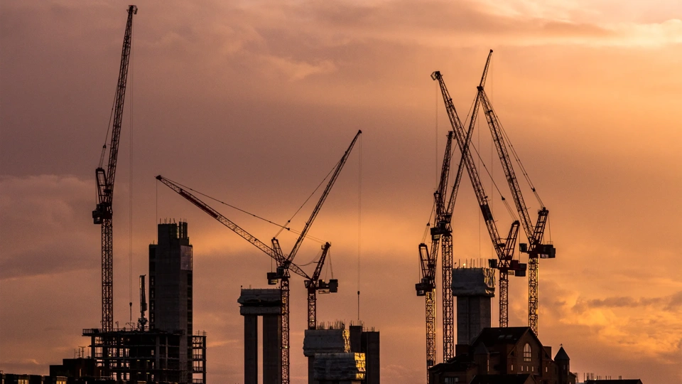 Color image depicting cranes and heavy duty construction equipment on the London skyline as the sun sets. The cranes have been busy constructing blocks of flats and apartments to ease the housing crisis in London and the south east of England. Lots of room for copy space.