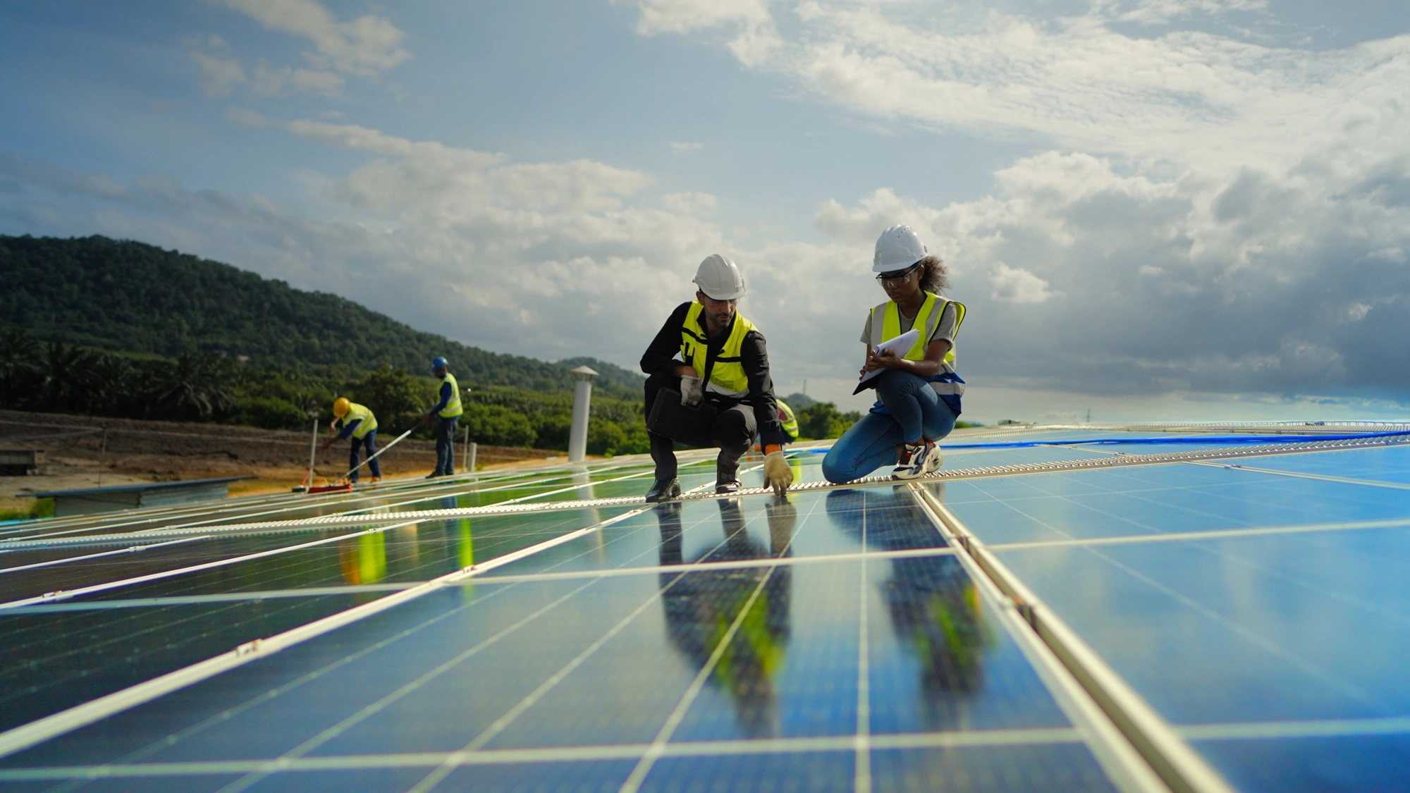 Team contractor, male engineer and female technicians wearing safety uniform, talking about installing plan, check the working system and maintenance solar panel of solar power plant to produce electricity on the roof of factory building. Industrial of renewable energy. Power generation from solar energy.