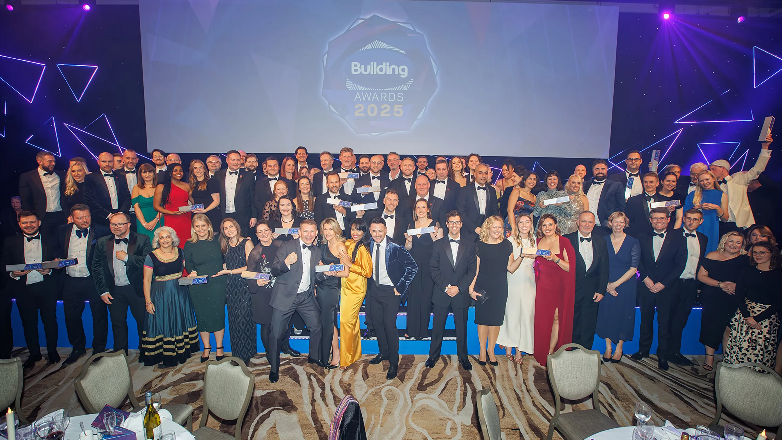 Turner & Townsend winners standing in front of billboard sign smiling at the building awards 2025
