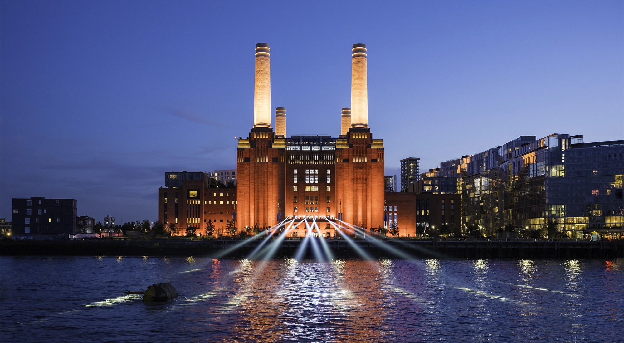 Battersea Power Station lit up at night, view from the Thames with buildings in the background
