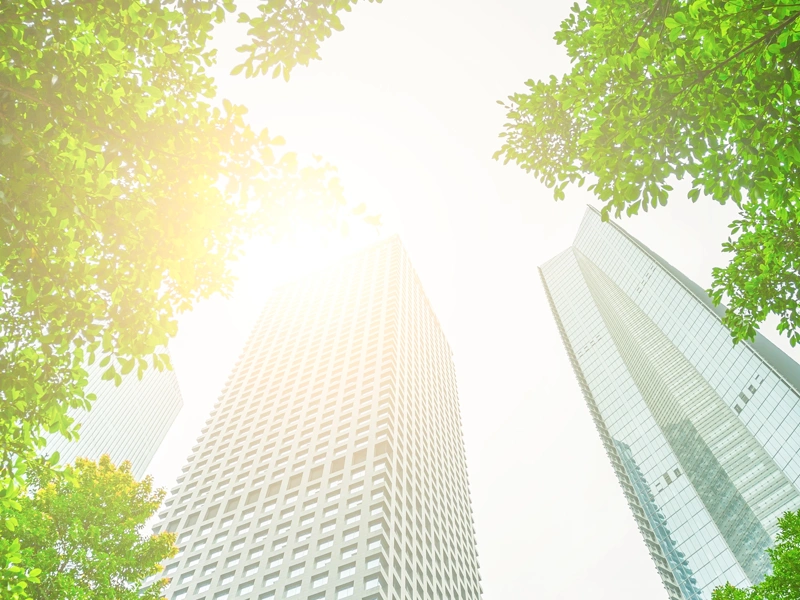 Two skyscrapers against bright sky with green trees either side
