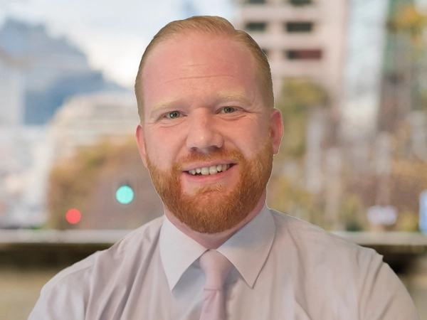 Portrait of Chris Robinson, Associate Director, Contract Services, outside in front of a blurred brown background featuring a building and mix of natural and urban elements.